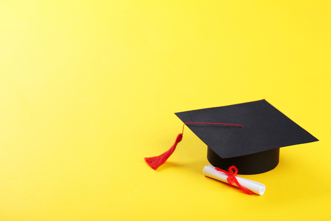 Graduation cap with diploma on yellow background